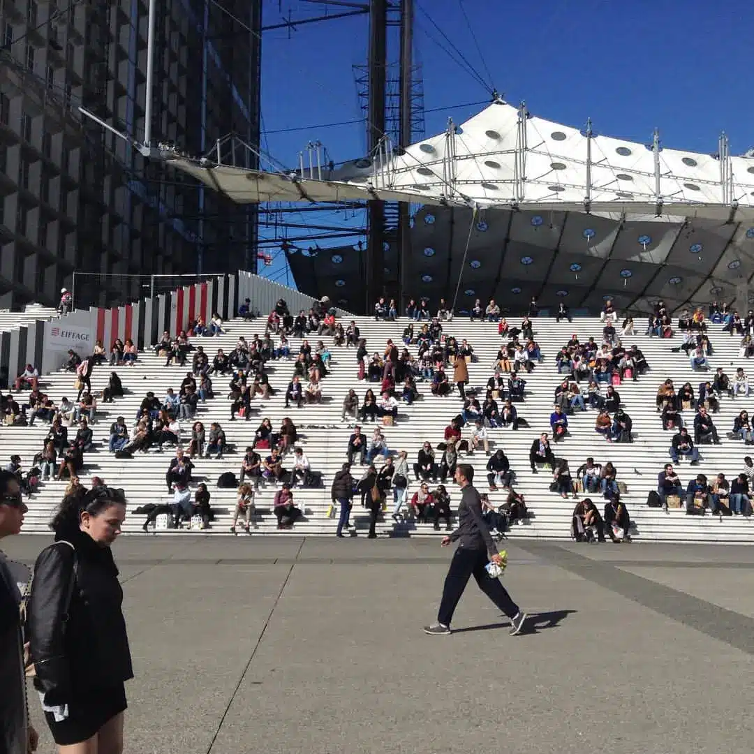 Photo du parvis de la Défense à Paris. Pause déjeuner avec un grand nombre de personnes assises sur les marches de l'Arche.